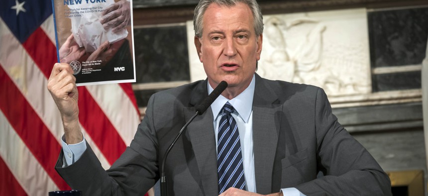 New York City Mayor Bill de Blasio at a press conference, holding up a pamphlet.
