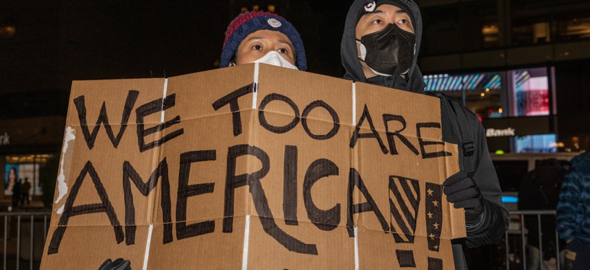 Two people holding up sign that say "We Too Are American!"