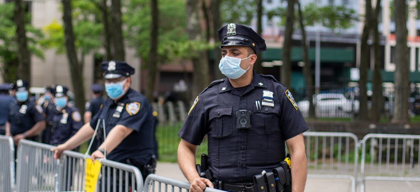 Masked New York City police officer stands at barricade.