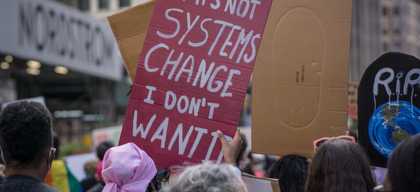 A protester in New York City holding a sign that says "If it's not systems change I don't want it."