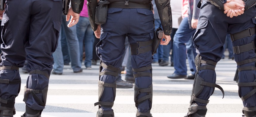 The lower halves of three police officers standing in a street.