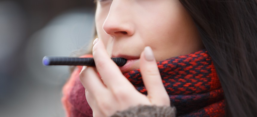 Young brunette holds e-cigarette between lips