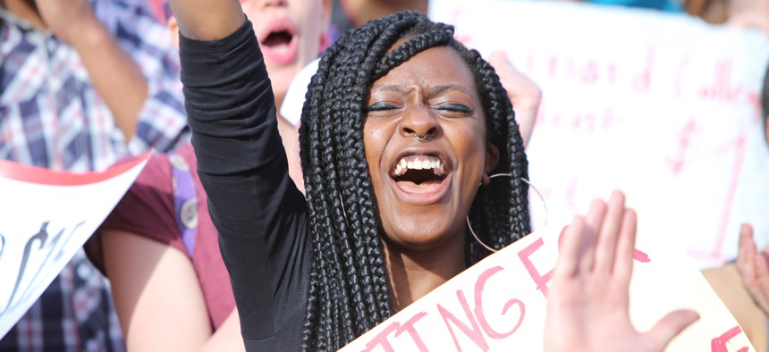 Woman raises her right fist while holding sign in middle of protest