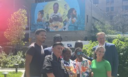 Dante de Blasio (in the back row, on the far left) and his father Bill de Blasio (also back row, far right) with artist Layqa Nuna Yawar, front row far left, pose with community members at the unveiling of “Colors of My City” at Vital Brookdale supportive housing complex in Brownsville, Brooklyn, on Friday. 