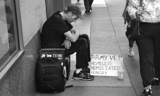 A man sits on a busy New York City sidewalk with a sign declaring he is a homeless military veteran.