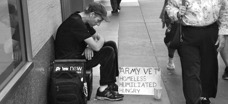 A man sits on a busy New York City sidewalk with a sign declaring he is a homeless military veteran.